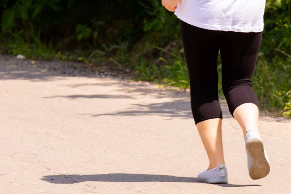 Beyaz tişörtlü ve siyah taytlı bir kadının, güneşli bir günde, vücudu sağlıklı tutmak için parkta egzersiz yaparken çekilmiş fotoğrafı.. — Stok fotoğraf