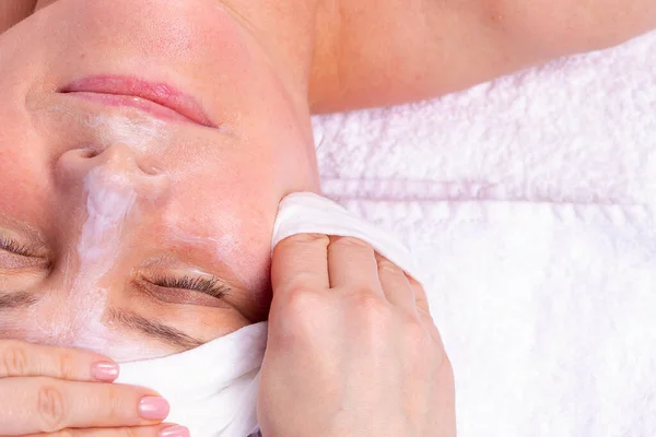 Close up side view zdjęcie kobiety otrzymującej pielęgnację twarzy przez kosmetyczkę w salonie spa, nakłada maskę kremową na twarz i zdejmuje ją. — Zdjęcie stockowe