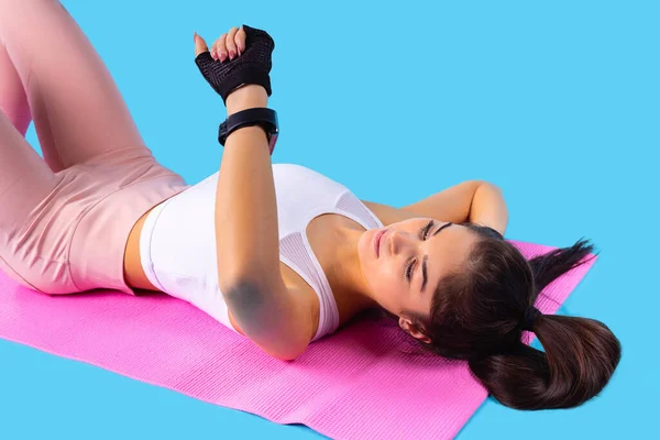 Jong fitness mooi meisje ligt op de fitness roze mat kijken naar het horloge op haar hand ze opvoeden. — Stockfoto