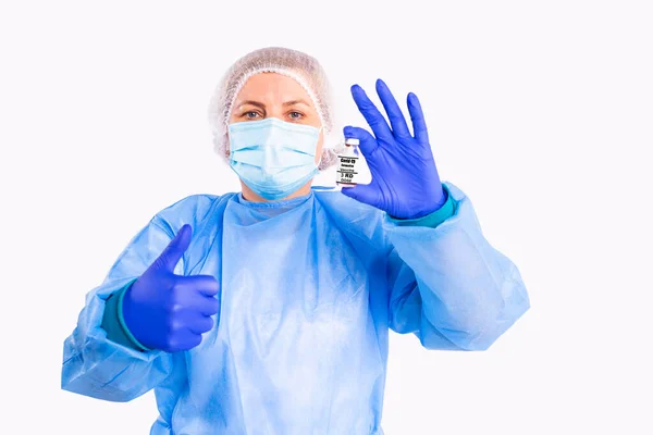 La foto de un médico en uniforme médico, mascarilla protectora y guantes sosteniendo en una botella de vacuna de la mano contra el coronavirus y con otra mano hace señal ok. — Foto de Stock