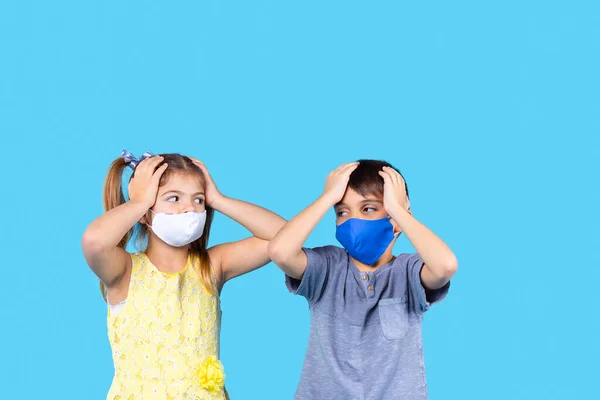 Two kids boy and girl in casual clothes wearing medical face masks use both hands to hold their heads due to headache and looking at each other. — Stock Photo, Image