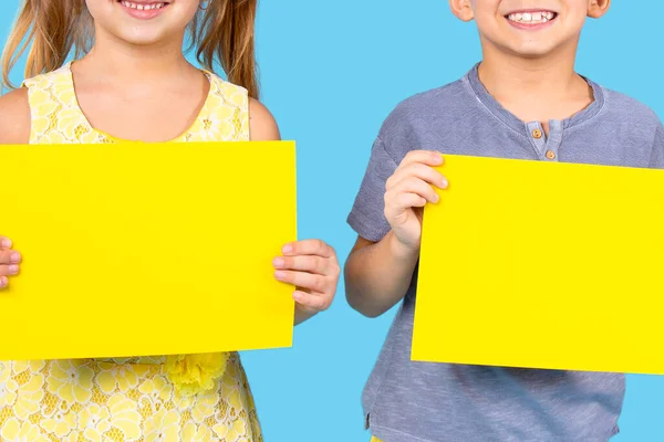 快乐的男孩穿着紫罗兰色的纽扣T恤，女孩穿着黄色花裙，蓝色背景上握着两张黄色的纸. — 图库照片