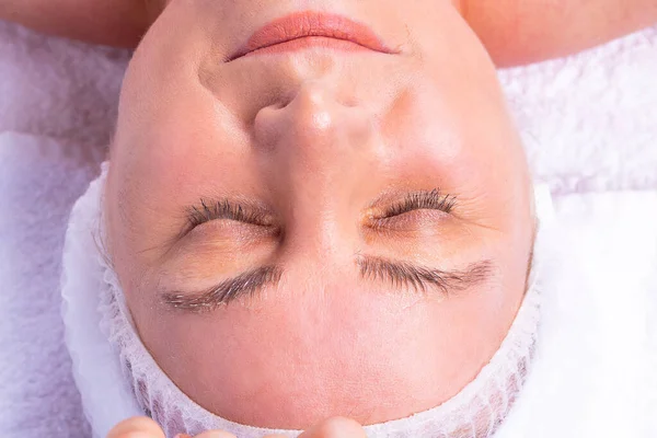 Close up foto de uma mulher no salão de spa deitado na mesa de massagem com os olhos fechados submetidos a um procedimento de descascamento facial. — Fotografia de Stock