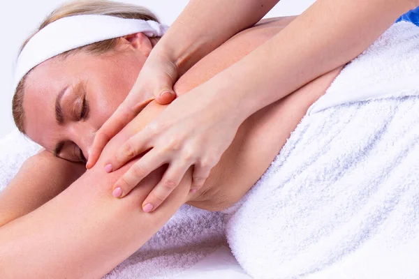 Close up photo of a woman being in a spa salon lying on the massage table with her hands under her head with closing eyes, undergoes a shoulder massage. — Stock Photo, Image