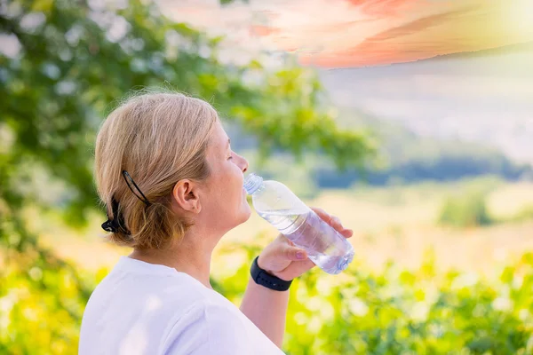 Femme blonde buvant un peu d'eau de la bouteille en plastique portant la montre numérique étant à l'extérieur et profitant de la journée d'été. — Photo
