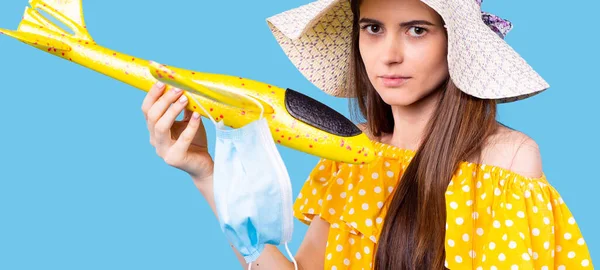 Letní čas dovolená dívka ve žlutých puntíkových šatech a plážový klobouk drží letadlo hračka s lékařskou maskou. — Stock fotografie
