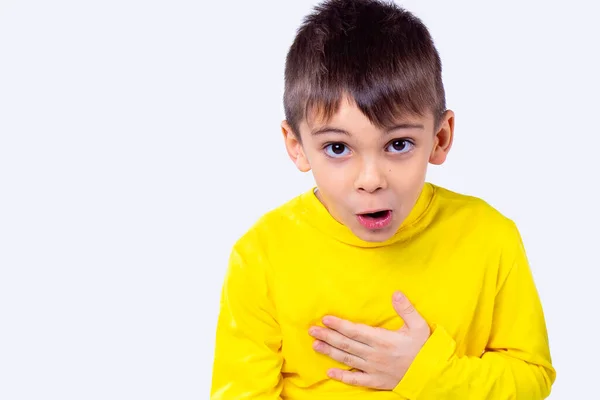 Foto de cerca de un niño con expresión de la cara sorprendida en cuello alto amarillo de manga larga sostiene su mano sobre su pecho. — Foto de Stock