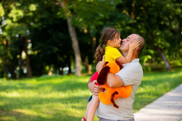 Αγαπώντας και φροντίζοντας τον μπαμπά κρατώντας την κόρη του στα χέρια του, αγκαλιάζοντας την κρατώντας το σκυλί μαλακό παιχνίδι στο χέρι του και το κοριτσάκι κρατά το κεφάλι του πατέρα της θέλει να του δώσει ένα φιλί. — Φωτογραφία Αρχείου