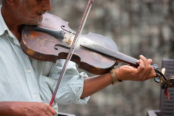 profile photo of an old man musician unshaven wearing stripped t-shirt holding in his hands violin and performing melodic music outdoors.