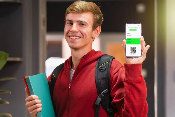 Lächelnder Studentenjunge mit Impfpass auf Mobilgerät. Zurück zu Universität, Schule, Hochschule gesundes und geimpftes Konzept — Stockfoto