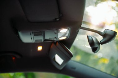 Ön camın ortasındaki döner aynanın içinde fotoğraf, içinde küçük ayna olan şoför için güneş koruması ve arabadaki ışığı kontrol etmek için düğmeler..