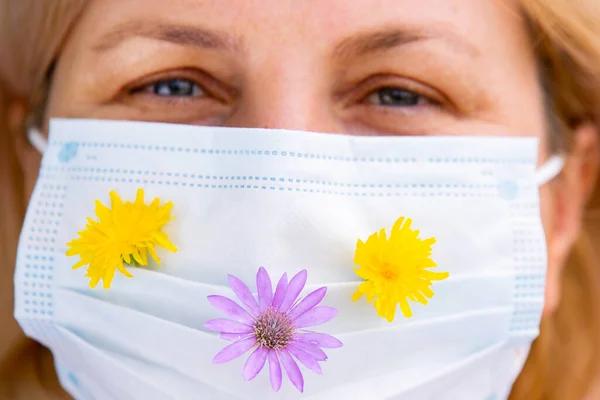 Närbild foto av en blond kvinna bär medicinsk mask med ängen blommor på den och tittar med trånga ögon . — Stockfoto