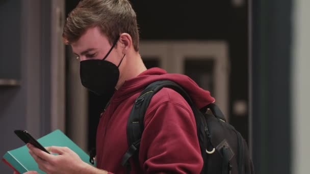 Student pojke bär skyddande svart ansiktsmask redo för lektioner som visar digitala vaccinationskort på den mobila enheten — Stockvideo