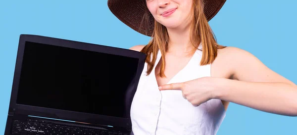 Piacevole donna bionda in breve top bianco e cappello che mostra schermo del computer portatile vuoto che punta su di esso con indice. — Foto Stock