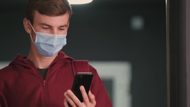 Студент у медичній масці, одягнений у светр, який показує картку вакцинації у своєму мобільному додатку, він рятується від вірусу . — стокове відео