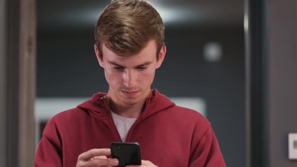 Primer plano de vídeo de un estudiante en sudadera con capucha roja buscando en su teléfono móvil certificado de vacunación internacional y mostrando en cámara. — Vídeo de stock