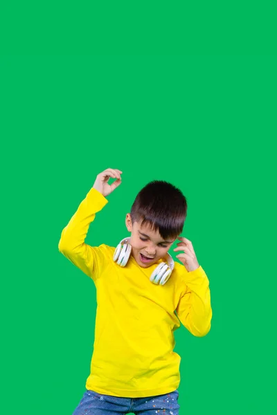 Chłopiec w żółtej koszulce i dżinsach trzymający białe słuchawki na ramionach i słuchający tańczącej muzyki. Przestrzeń nad zdjęciem. — Zdjęcie stockowe