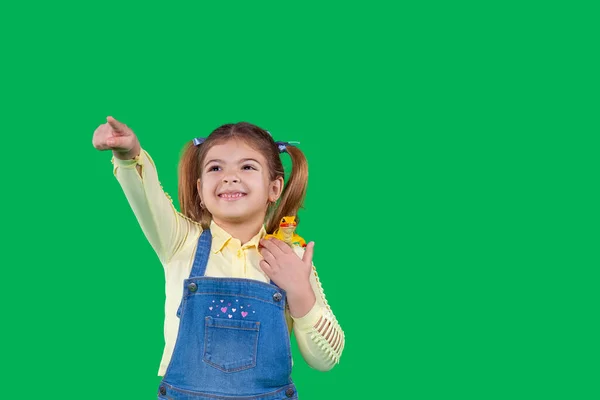 Hermosa niña sonriente en ropa de mezclilla y con la cola de dos en la cabeza está apareciendo con la mano. — Foto de Stock