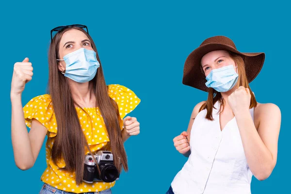 Satisfeito duas jovens mulheres morena e loira em máscaras médicas vestindo chapéu e óculos de sol dançando olhando para cima. — Fotografia de Stock