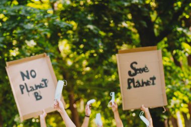 Yeşil parktaki çevre mitinginde, dünya gezegenini kurtarmak için kirliliği ve küresel ısınmayı protesto eden insanlar, salgın zamanında tıbbi maskeleri yükseltmek için ev yapımı posterler..
