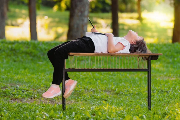 Foto de uma jovem deitada em um banco nas costas segurando o telefone inteligente na mão, descansando após o trabalho de limpeza voluntário ao ar livre. — Fotografia de Stock