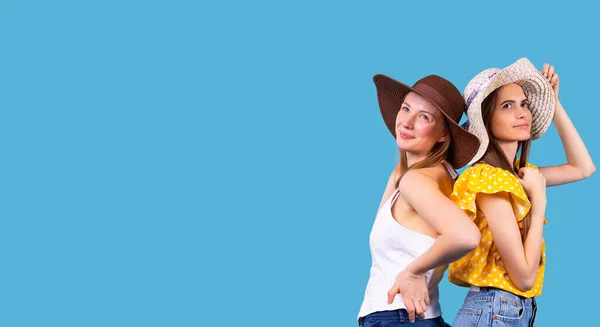 Dvě úžasné mladé ženy v kloboucích stojící zády k sobě a s úsměvem vzhlížející tváří. — Stock fotografie