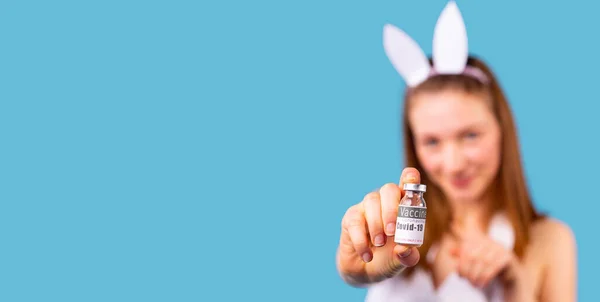 Närbild av en ung dam som bär båge med hare öron på huvudet och visar flaskan med vaccin. — Stockfoto