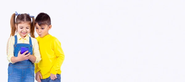 İki çocuk gülümsüyor ve şaşırmış ifade ekrana bakıyor, oyun oynuyor veya uygulama kullanıyor. 