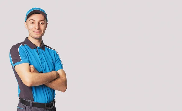 Homem de entrega ter expressão rosto alegre vestindo uniforme carteiro azul de pé com as mãos cruzadas, espaço vazio lateral. — Fotografia de Stock