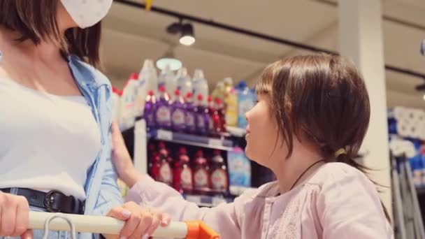 Situación en la tienda, chica bonita embolsando a su madre en una máscara médica para comprar sus dulces y mostrando con la mano a un lado con los estantes. — Vídeo de stock