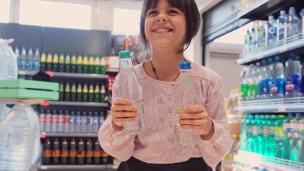 Joyful meisje dansen in de voorkant van de stand met de flessen in de winkel met twee flessen in haar handen en het opvoeden van hen. — Stockvideo