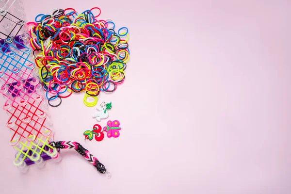 Colored rubber bands for weaving bracelets, toys. Loom for weaving toy bracelets from elastic bands. The child weaves a bracelet from elastic bands.