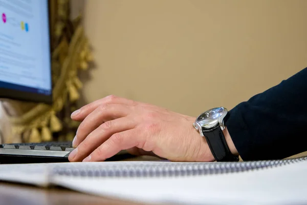 Businessman working on computer, hand with clock close up.