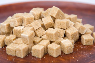 Tahta bir tabakta kahverengi şeker küpleri beyaz bir arka planda yakın plan