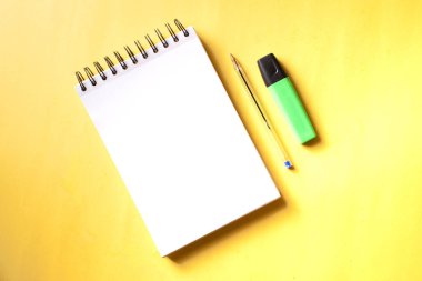 Üst görünüm yüzük klasörü dizüstü, kalem ve fosforlu yeşil, sarı bir arka planda yan yana..