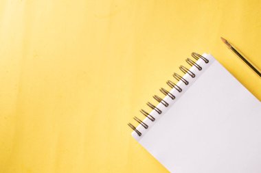 Üst Manzara. Beyaz kâğıtlı yüzük defteri ve sarı arka planda bir kalem. Uzayı sola kopyala