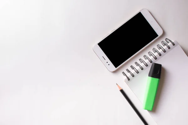 top view of a ring notebook with a phosphorescent green highlighter, a pencil on the left of the notebook and a mobile phone on the top right. The whole image is composed on the right, leaving a copy space on the left.