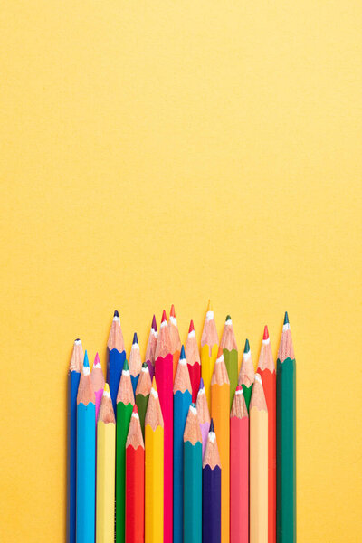 Top view. Pencils are colored on top of each other and next to each other on a yellow background and pointing upwards where there is a copy space.