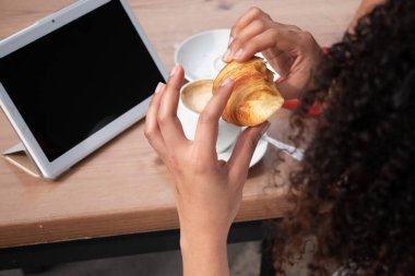 Arka planda kruvasan yiyen bir kız bir tablet ve bir kahveydir. Geri çekim.