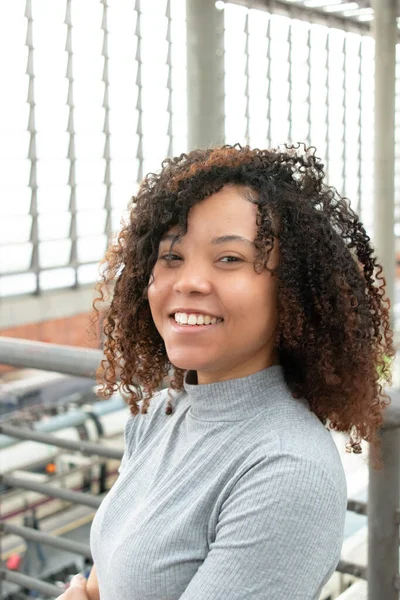 young black woman in gray t-shirt looking at smiling camera while touching her hair.