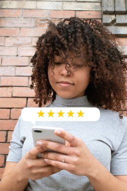 Kıvırcık saçlı kız, beş yıldızlı bir servis deneyimini değerlendirmek için akıllı telefon kullanıyor. İş konsepti.