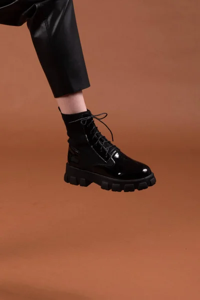 Deri pantolon ve çizme giymiş, kahverengi arka planlı bir stüdyoda tanınmayan birinin bacağı..