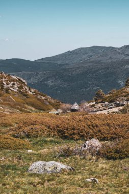 Ortasında küçük bir kulübe olan bir dağ manzarasının fotoğrafı..