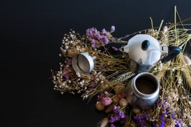 Kahve yapma konsepti. Moka kahve yapmak için gerekli malzemeler. Koyu arka planda kahve ve renkli çiçeklerle moka demliği. Kahve klasik bir estetik kompozisyonda..