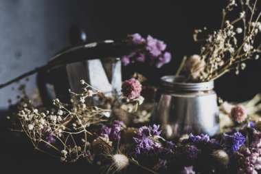 Kahve yapma konsepti. Moka kahve yapmak için gerekli malzemeler. Koyu arka planda kahve ve renkli çiçeklerle moka demliği. Kahve klasik bir estetik kompozisyonda..