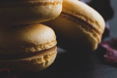 Sarı badem kurabiyeli limonlu kahvaltı sabahı yakın plan. Siyah arka planda Fransız tatlısına yakın plan ve çiçekler basit bir klasik kompozisyonda. Yemek fotoğrafçılığı.