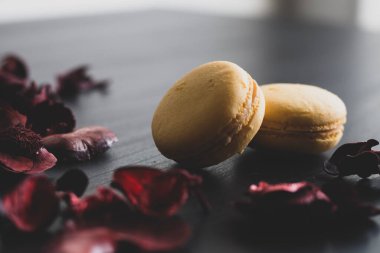 Sarı badem kurabiyeli limonlu kahvaltı sabahı yakın plan. Siyah arka planda Fransız tatlısına yakın plan ve çiçekler basit bir klasik kompozisyonda. Yemek fotoğrafçılığı.
