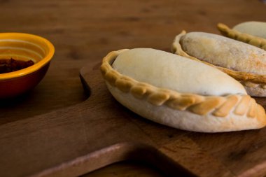 Geleneksel pişmiş Arjantin börekleri et dolması ya da ahşap arka plan ve baharatlı sosa karşı sebzeli lezzetli hamur işleri. Latin Amerika Kızarmış Yemekleri.