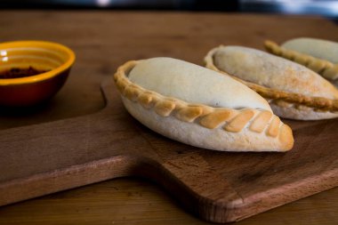 Geleneksel pişmiş Arjantin börekleri et dolması ya da ahşap arka plan ve baharatlı sosa karşı sebzeli lezzetli hamur işleri. Latin Amerika Kızarmış Yemekleri.