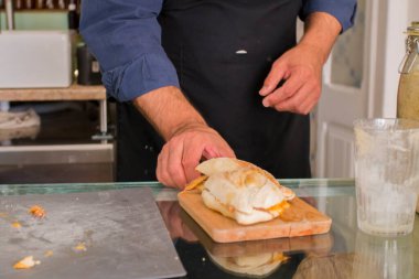 İspanyol erkek ellerinin soslu, geleneksel bifana soslu ve empanadalı, geleneksel latin yemekli ekmek sandviçi keserken ve yaparken üst görüntüsü. Sandviç yapma süreci.